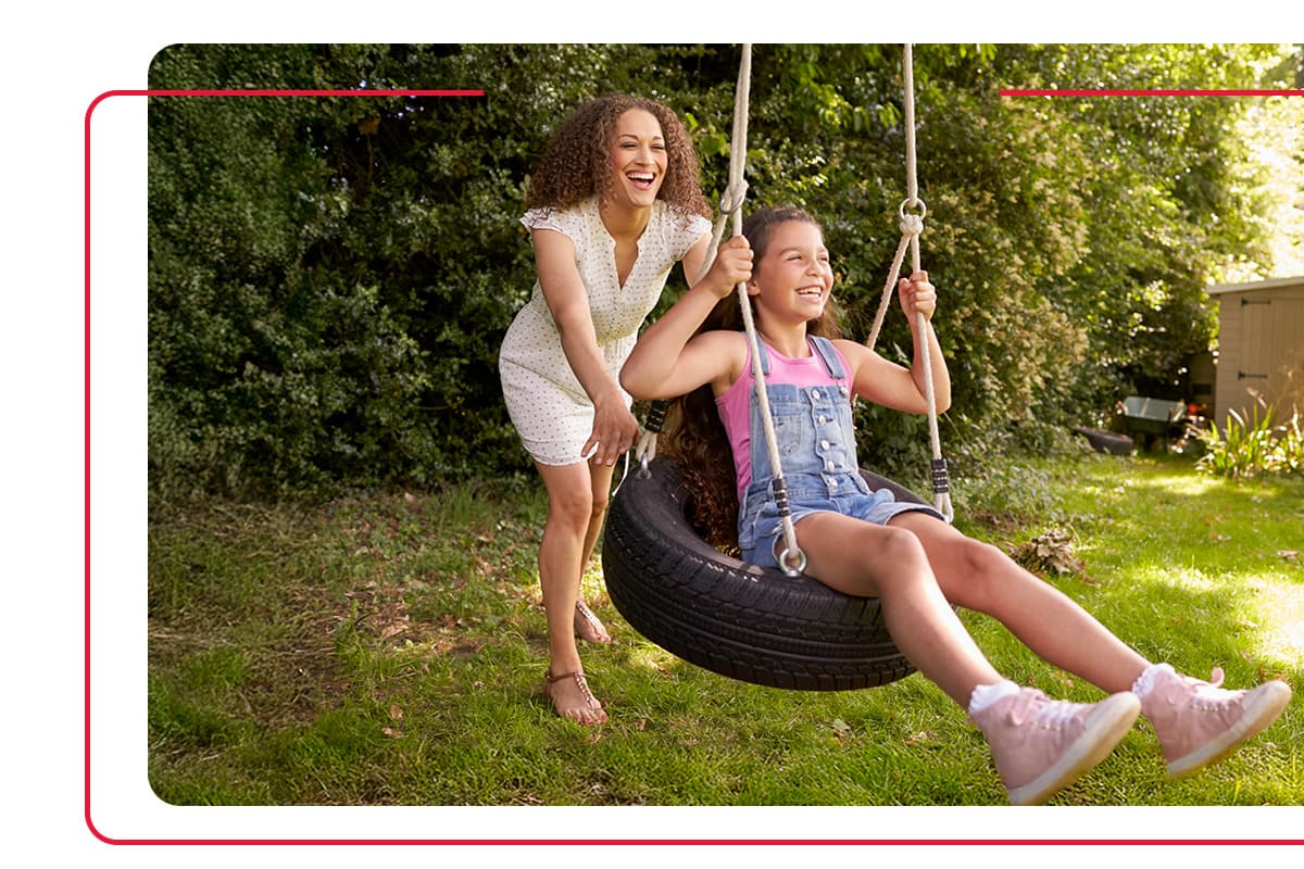 Mother pushing her daughter in a tire swing in their backyard