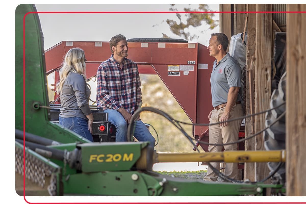 Farm Bureau Insurance of Tennessee agent meeting with family farmers next to farm equipment in barn