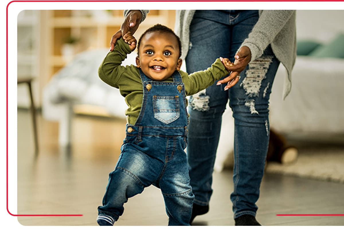 Young child learning how to walk with the help of the child's mother