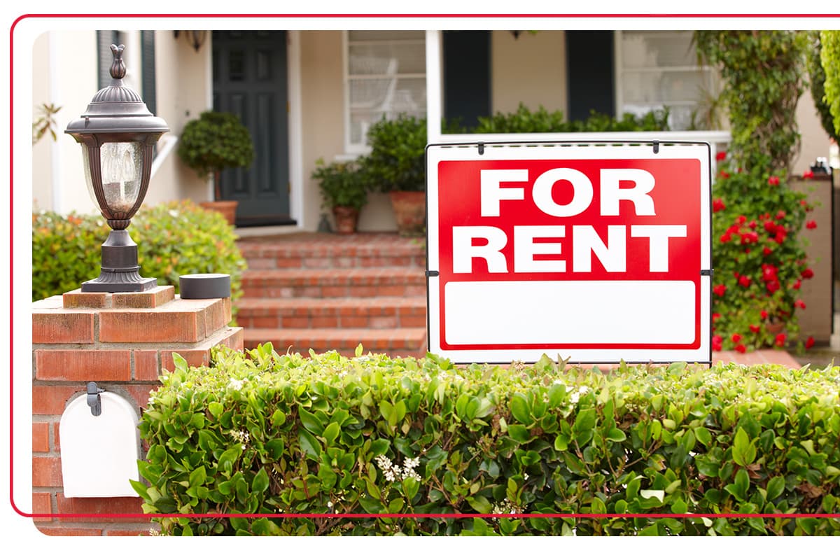 Red "For Rent" sign sitting in the front yard of a rental property house
