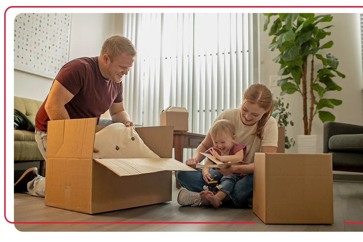 Young parents playing with their young child next to packing boxes in the living room of their home