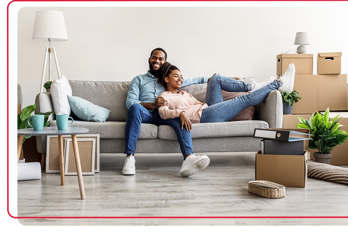 Young couple sitting on the couch in the living room of their house, surrounded by packing boxes