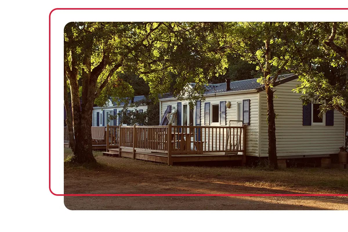 Mobile home with white siding and front porch sitting underneath large trees