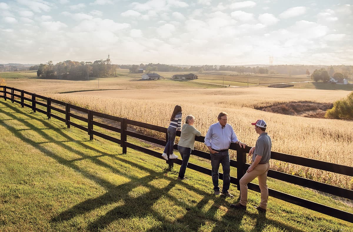 Tennessee family meeting with a Farm Bureau Insurance of Tennessee agent while leaning against the fence on their family farm
